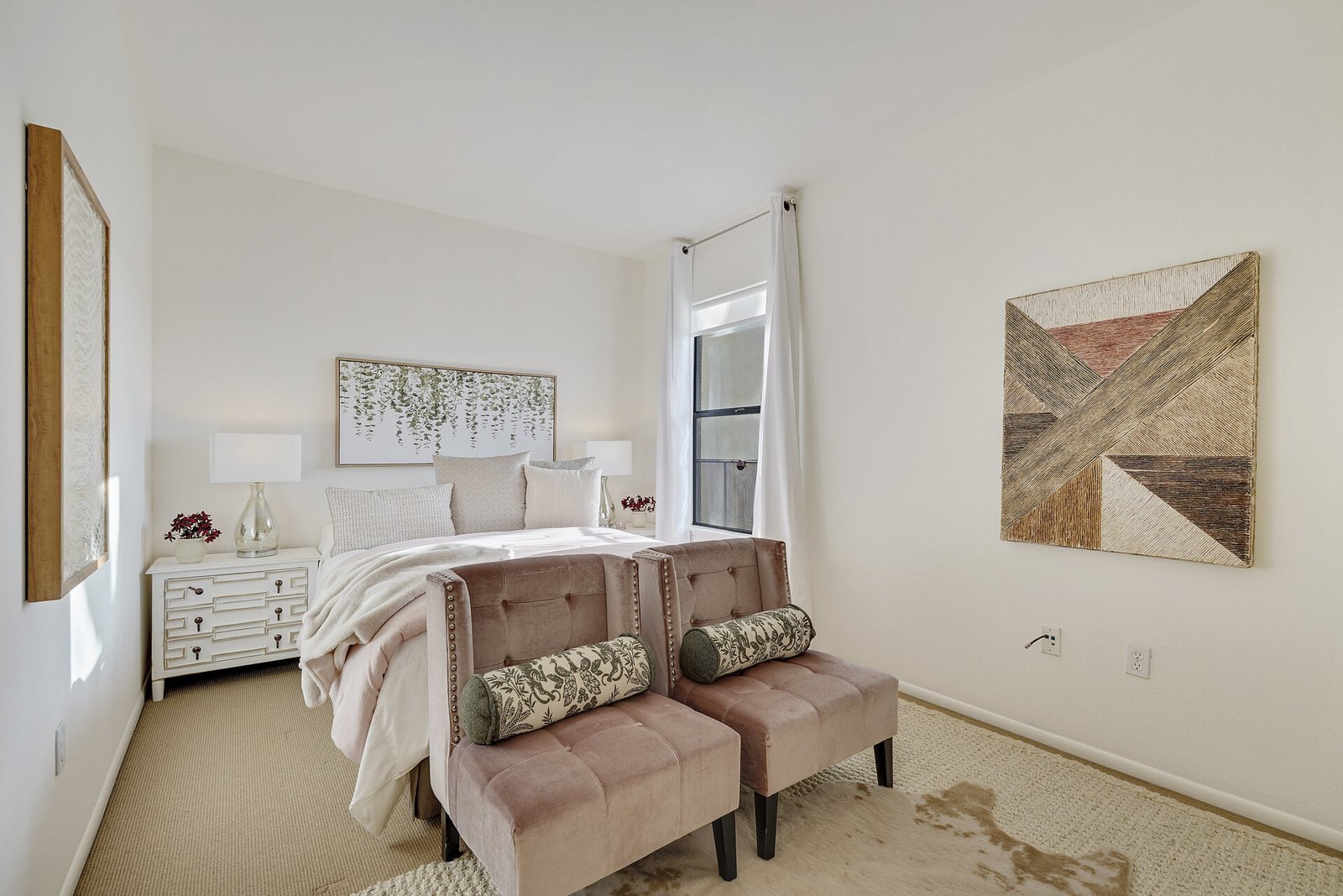 Bright bedroom with white walls, a bed with floral art above the headboard, and two velvet benches