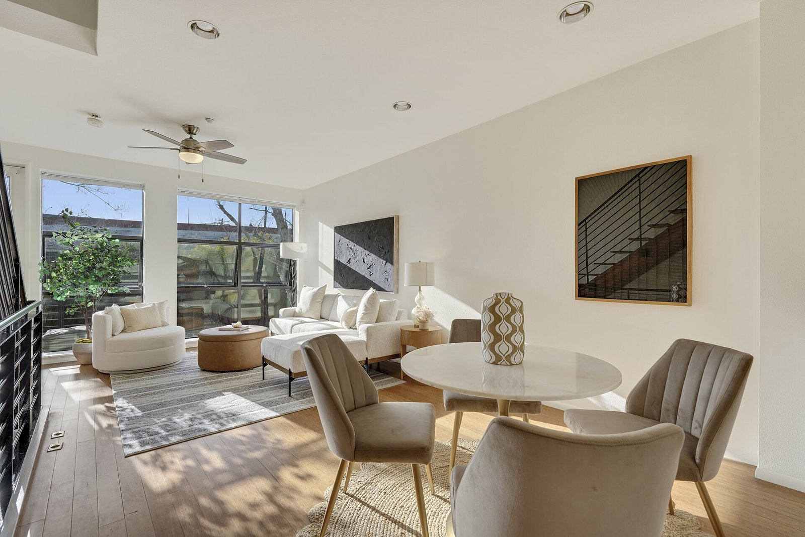 Open-concept living and dining area with a round white table, grey chairs, a white sofa, and large windows.