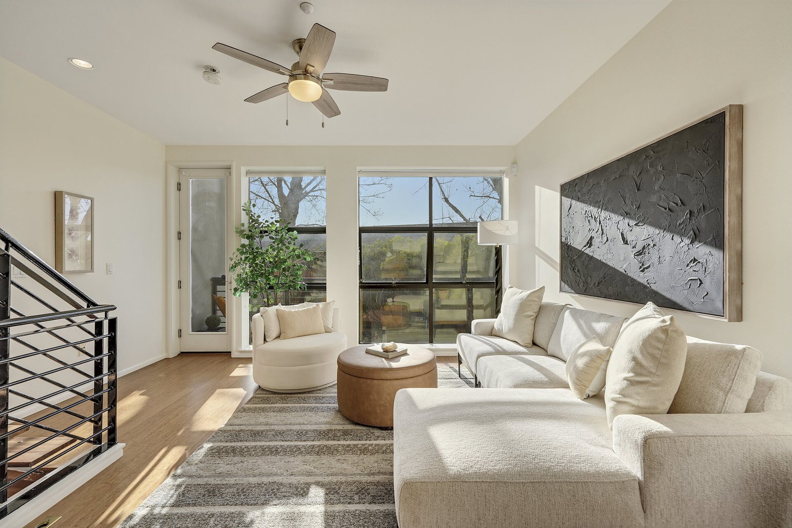Living room featuring a large white l-shaped sofa, a round leather ottoman, and a large black textured art piece on the wall.