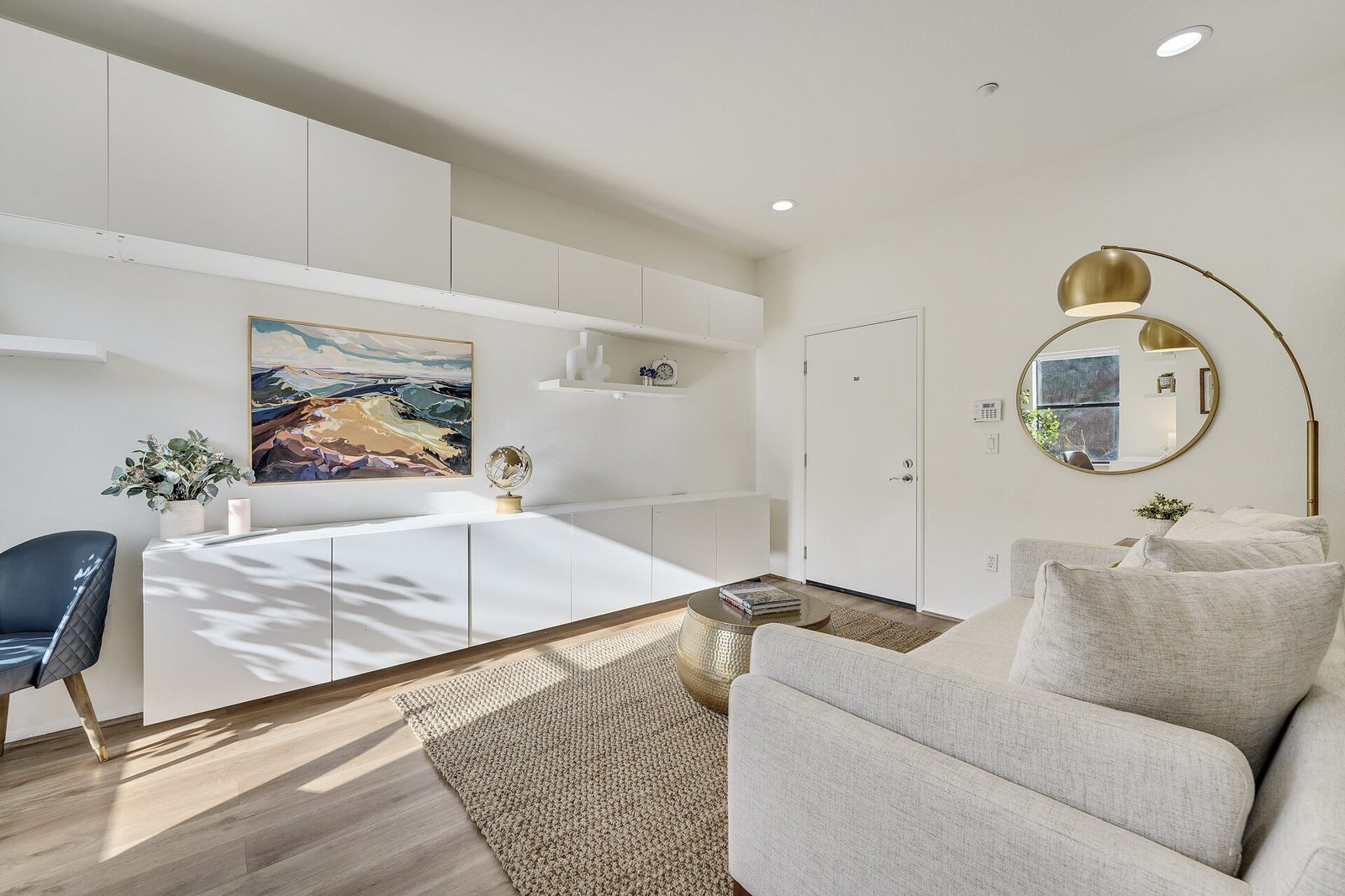 iving area with white cabinetry, a large mountain landscape painting, and a round gold mirror on the wall.