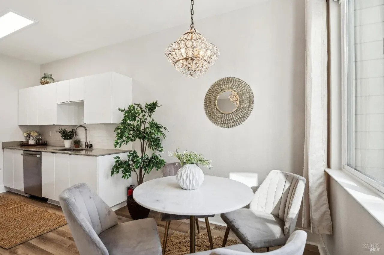 Modern kitchen and dining corner with white cabinetry, a round marble-top table, and a tiered crystal chandelier.
